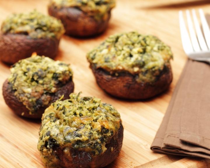 Five stuffed mushrooms with spinach and feta on a wooden board, a fork nearby.
