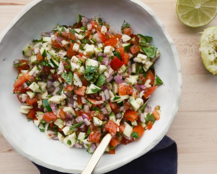 Fresh salsa with diced tomatoes, zucchini, onions, and herbs in a white bowl, with lime.