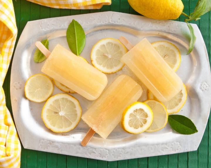 Four refreshing lemon popsicles on a silver tray with lemon slices and leaves.