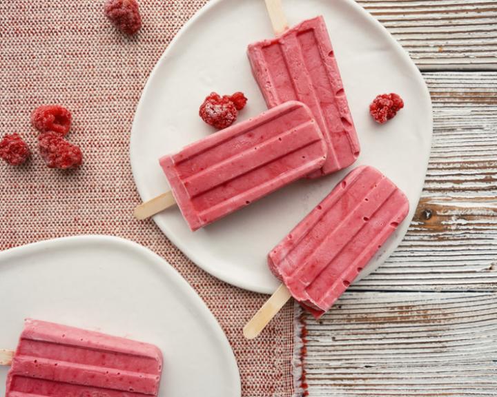 pink raspberry popsicles on white plates with scattered berries.