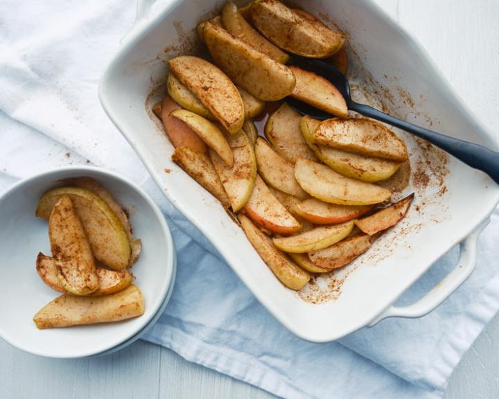 Baked apple slices with cinnamon in a white baking dish and bowl.