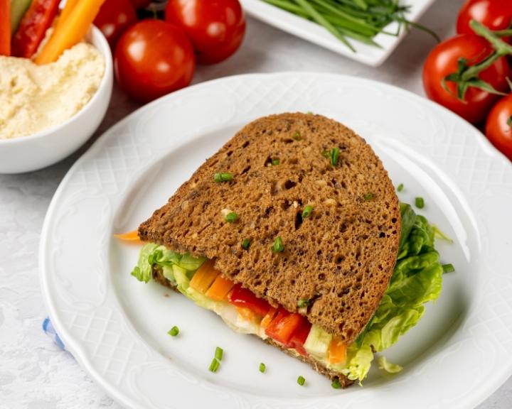 Sandwich on wheat bread with lettuce, colorful bell peppers, hummus