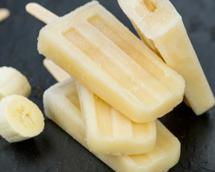 Banana popsicles stacked with banana slices on a dark background.