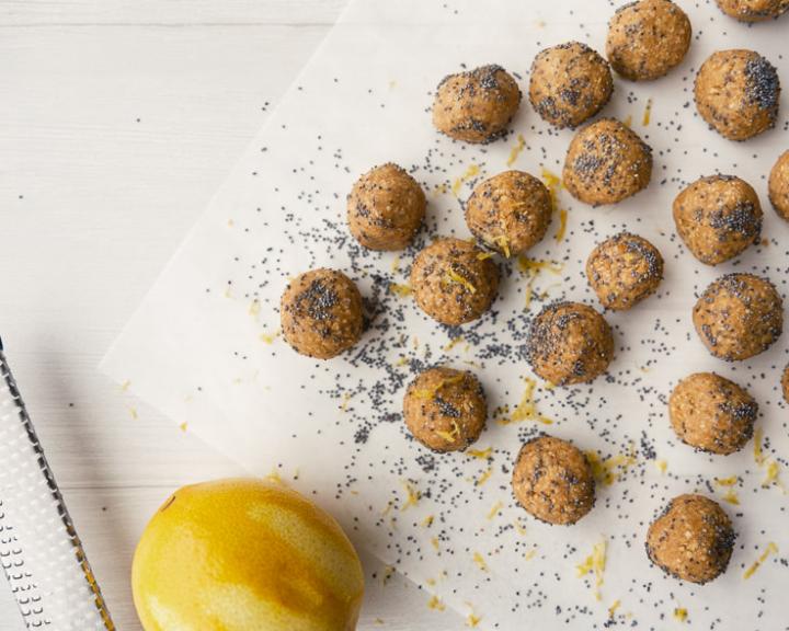 Lemon poppy seed energy bites on parchment paper with a fresh lemon.