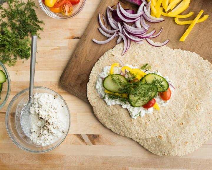 Healthy wrap with creamy spread, cucumbers, tomatoes, yellow peppers, and fresh dill.