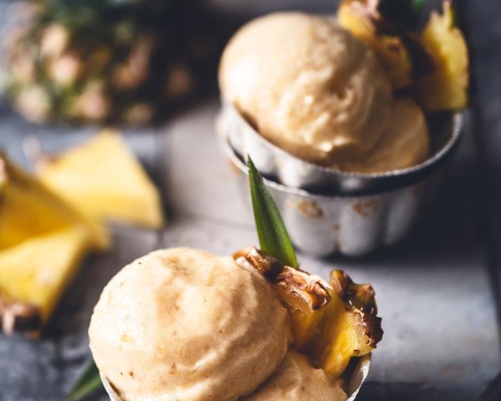 Scoops of light yellow pineapple frozen dessert garnished with fresh pineapple pieces.