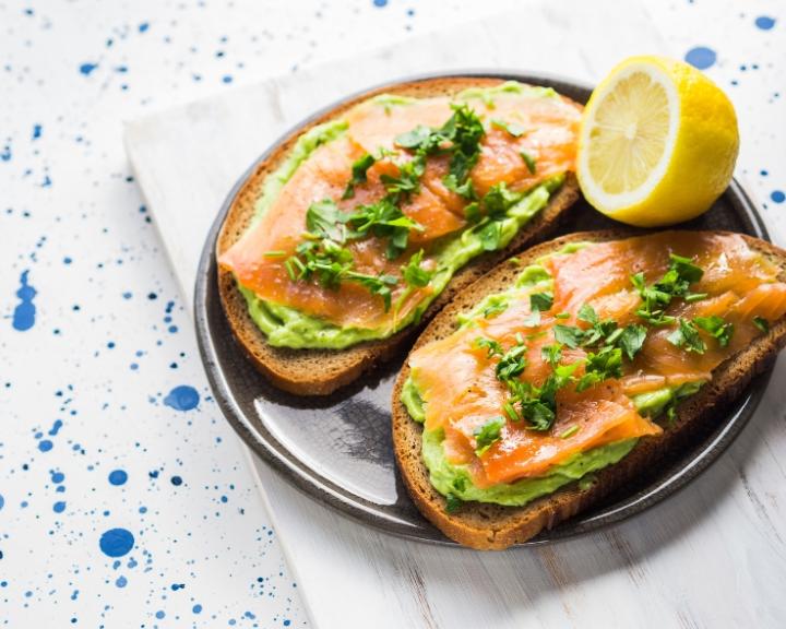 Two slices of toast topped with mashed avocado, smoked salmon, and herbs