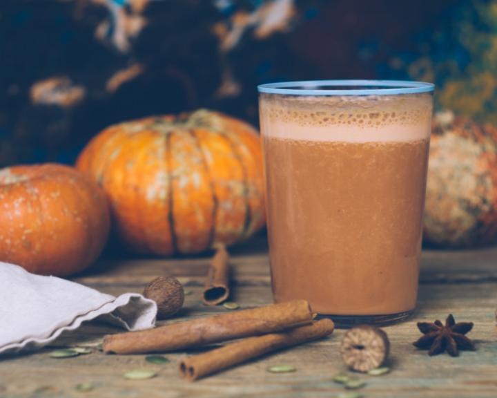 pumpkin almond smoothie in a glass with cinnamon sticks and pumpkins in the background