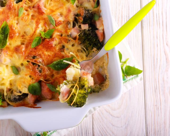 Cheesy broccoli and ham casserole in a white dish, with a serving fork.