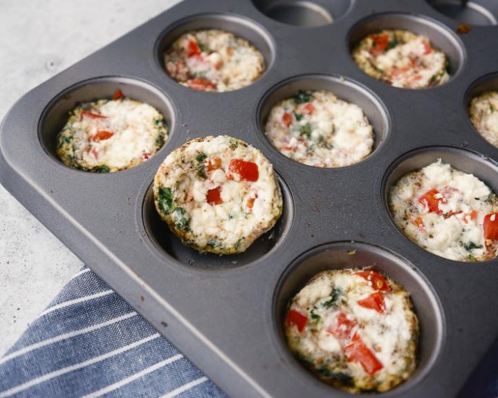 Healthy egg bites with red pepper and greens in a muffin tin.