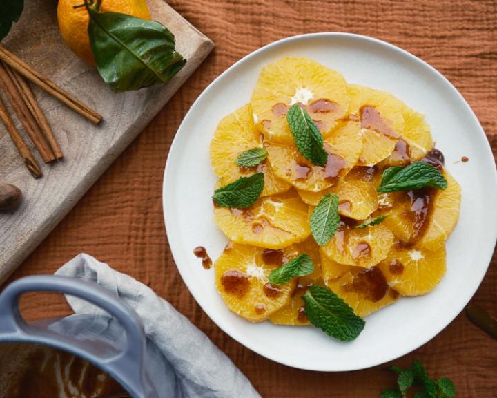 Fresh sliced oranges with mint and drizzle on a white plate. Spices nearby.