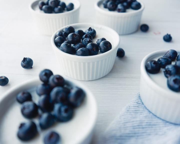 Small white bowls of yogurt mousse topped with fresh blueberries on a light surface.