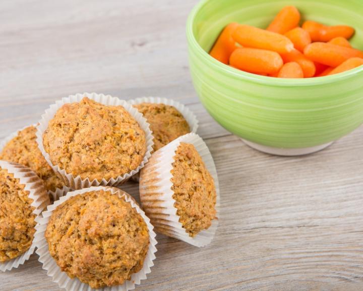 Muffins in white liners next to a green bowl of baby carrots.