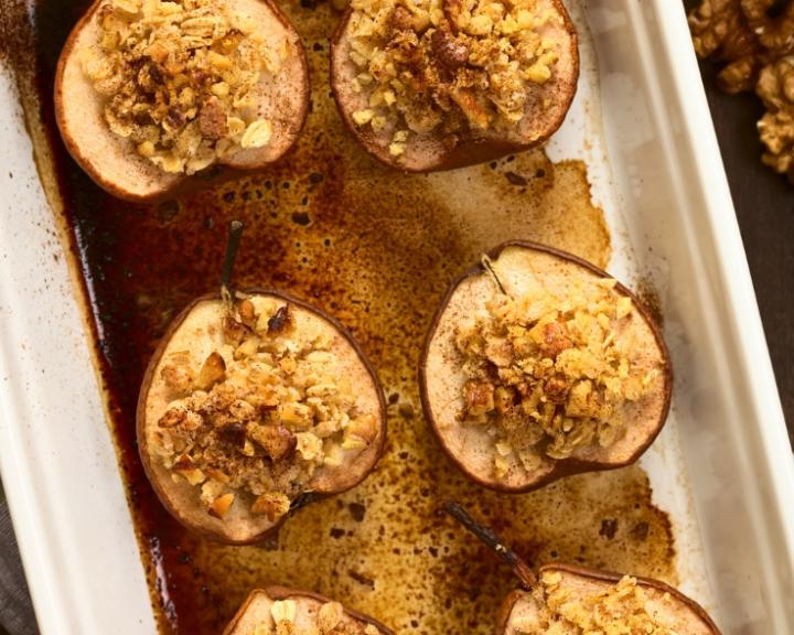 Halved baked pears with golden oat and nut topping in a white baking dish.