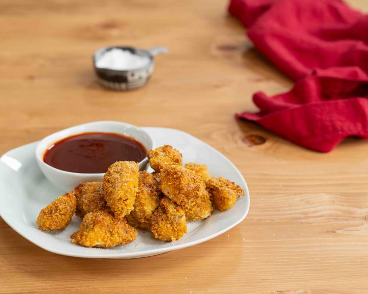 Golden chicken nuggets with barbecue sauce on a white plate, wooden table.