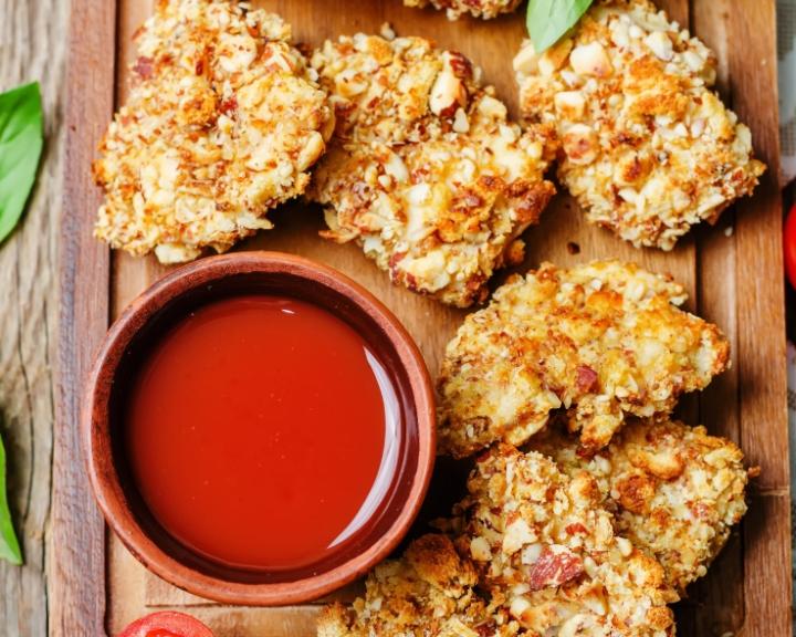 Crispy chicken nuggets with nutty crust and a small bowl of red dipping sauce.
