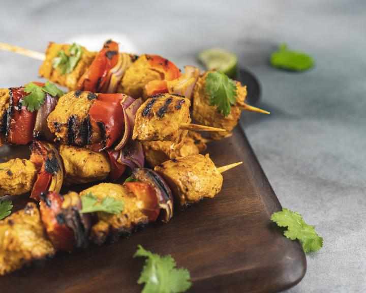 Grilled chicken and vegetable skewers with bell peppers and onions on a wooden board.