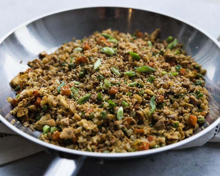 Cauliflower fried rice with vegetables and green onions in a large silver pan.