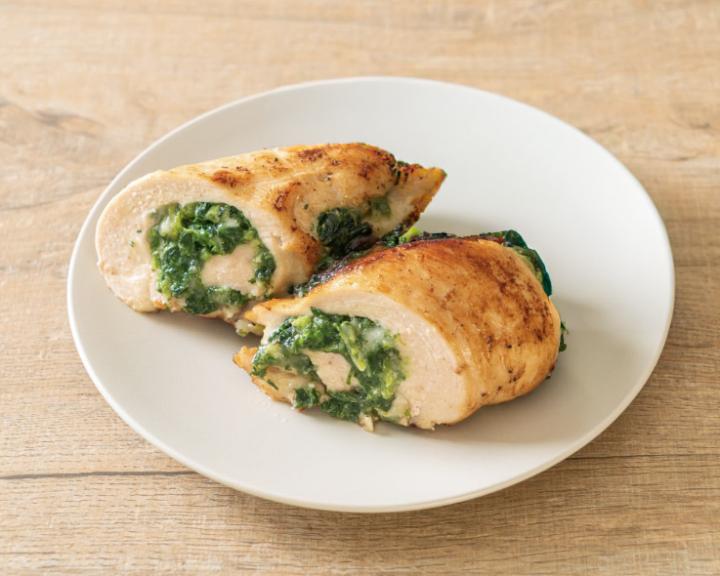 Two baked chicken breasts, sliced to show a green spinach filling, on a white plate.