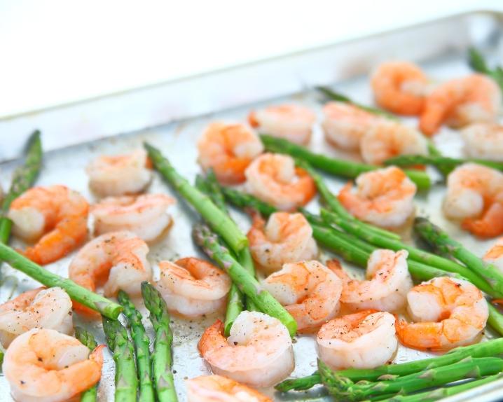 Cooked shrimp and asparagus spears on a metal baking sheet.