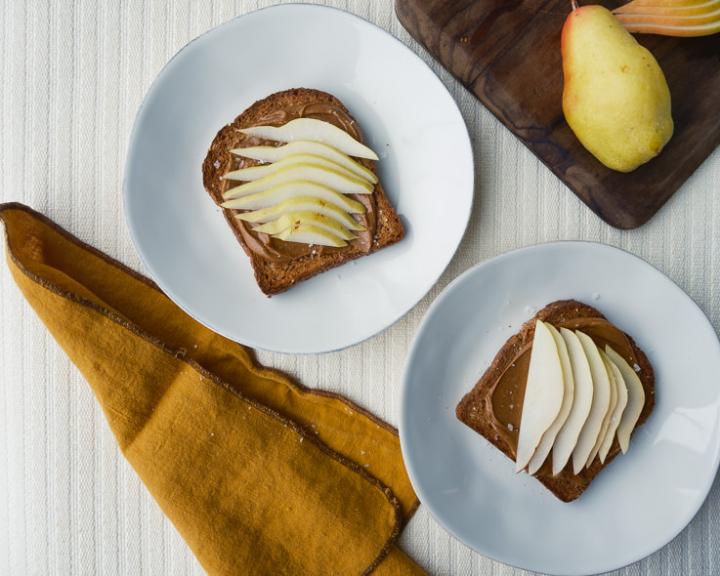 Toast with spread and sliced pears on white plates; whole pears on a board.