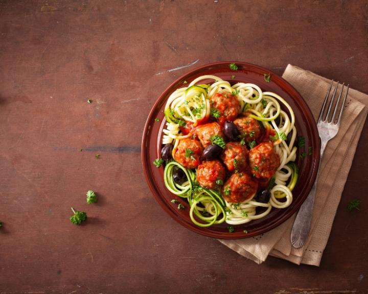 Plate with zucchini spaghetti, meatballs, tomato sauce, and black olives.