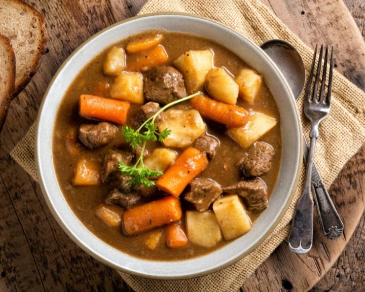 Bowl of hearty beef stew with meat, carrots, potatoes, and parsley garnish.