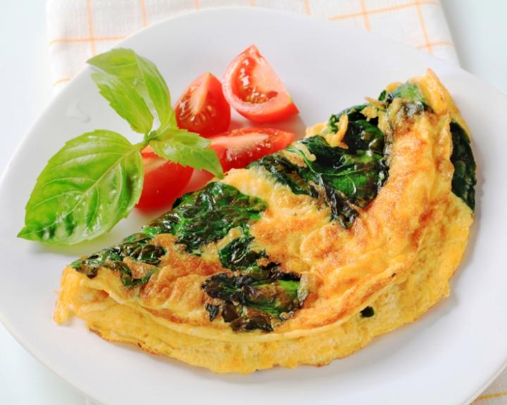 Tomato and basil omelet with tomato wedges and basil on a white plate.