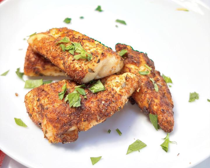 Seasoned chicken tenders with fresh parsley on a white plate.