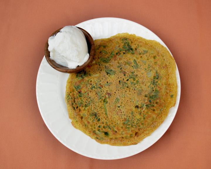 Savory pancake on a white plate with a side of yogurt.