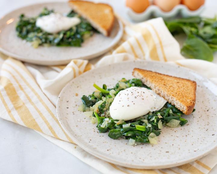 Two plates with sautéed spinach, onions, poached eggs, and toast. Eggs in background.