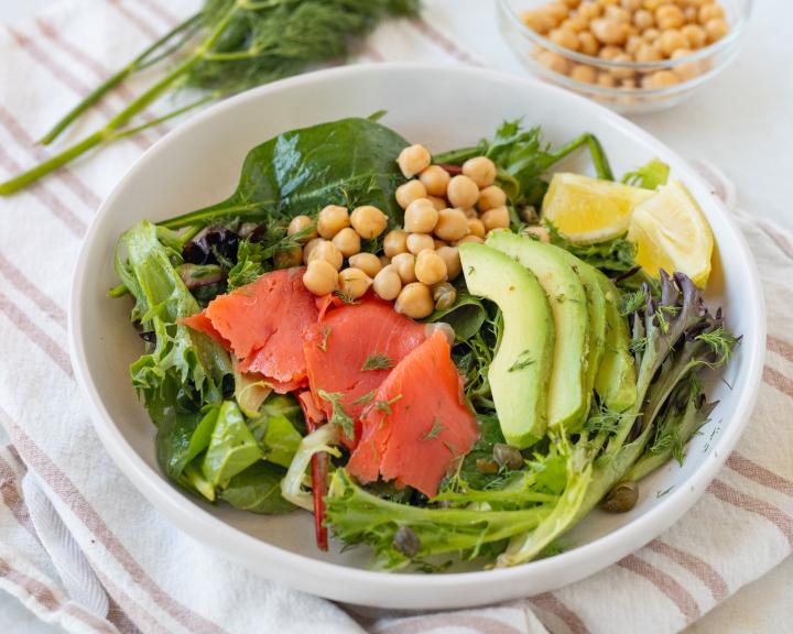 Bowl of mixed greens salad with salmon, avocado, chickpeas, and lemon.