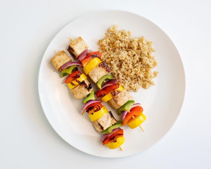 Two grilled tofu and colorful vegetable skewers with brown rice.